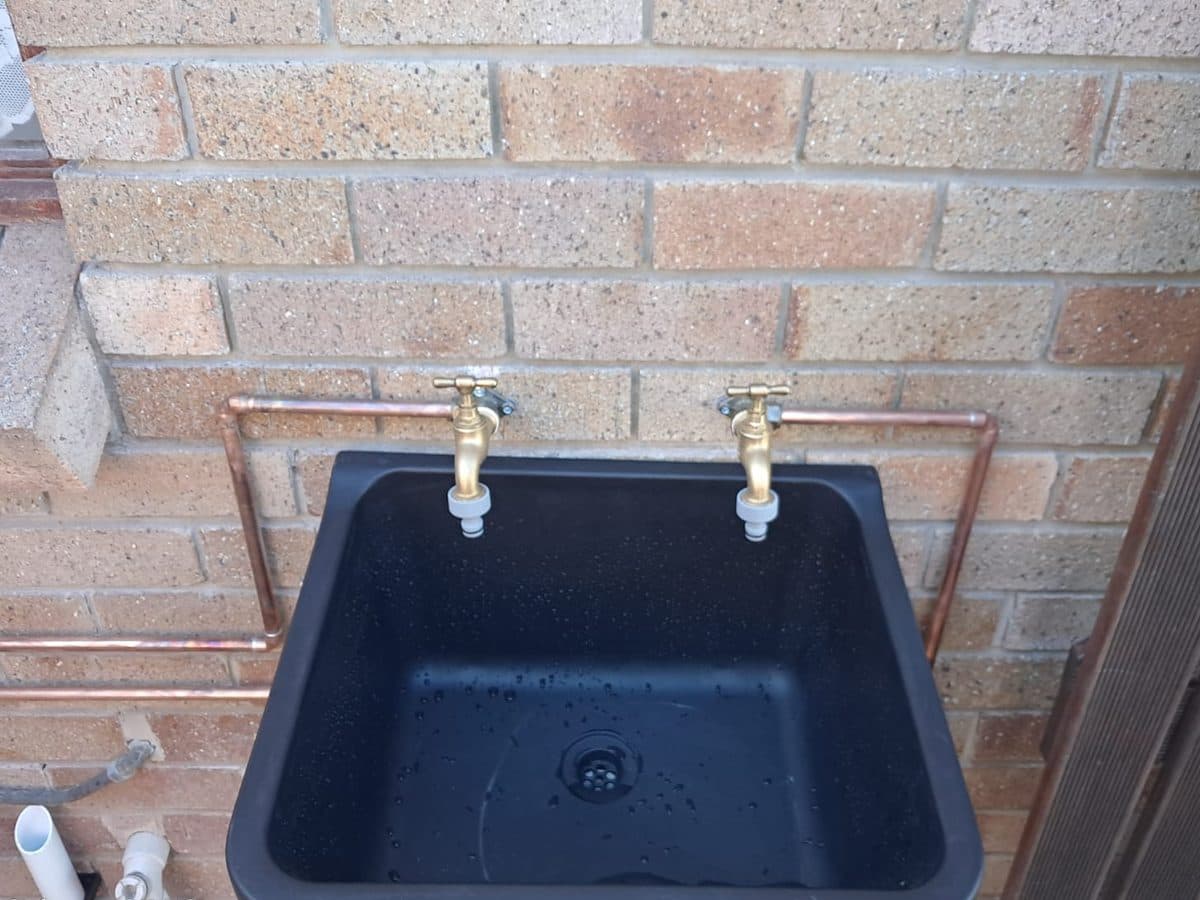 Laundry sink and taps fitted against a brick wall
