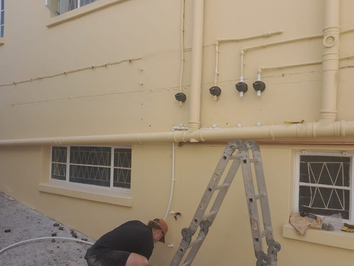 Technician on a ladder working on building pipework