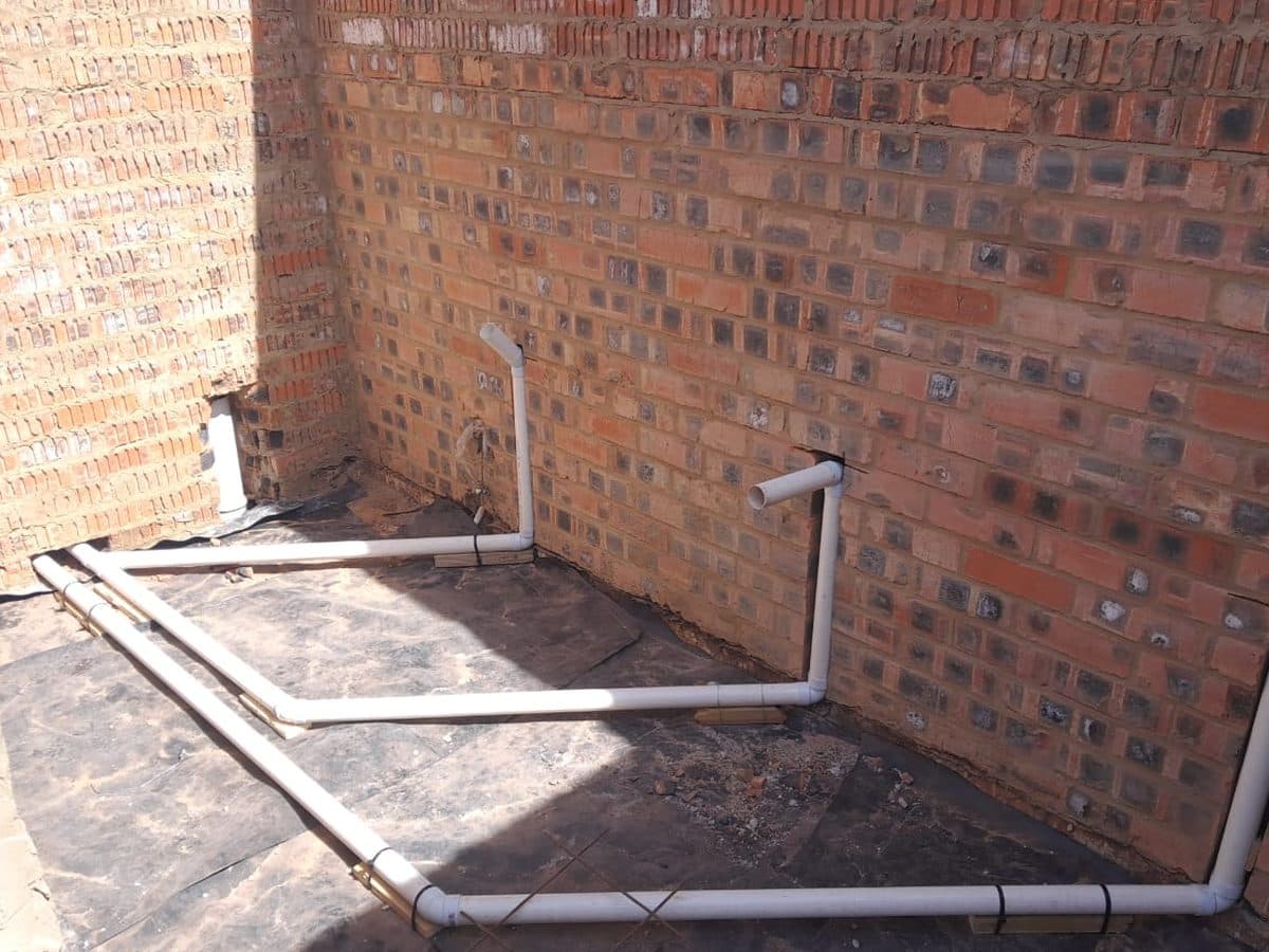 Pipework laid in a floor channel beside a brick wall